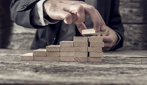 Man in a suit builds a staircase from wooden blocks on a wooden table