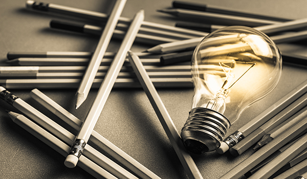Glowing light bulb surrounded by scattered pencils